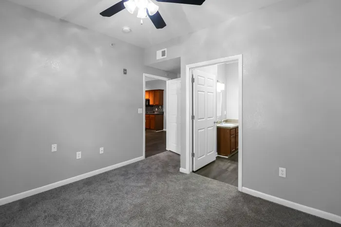 Modern apartment room with plush carpet, efficient ceiling fan, and open view to kitchen and bathroom.