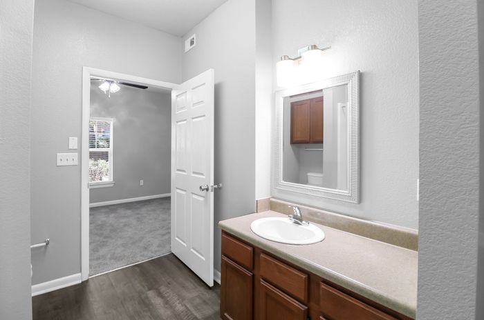 Bright and modern bathroom with elegant vanity, featuring a view into a cozy carpeted bedroom through an open door.