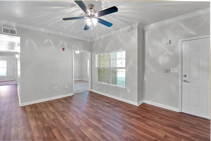 Inviting open-concept apartment showcasing elegant wood flooring, modern ceiling fan, and abundant natural light from large windows.