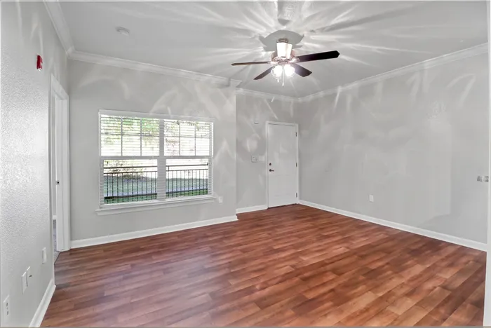 Bright and inviting living room with modern ceiling fan, stylish wooden flooring, and large window offering natural light.