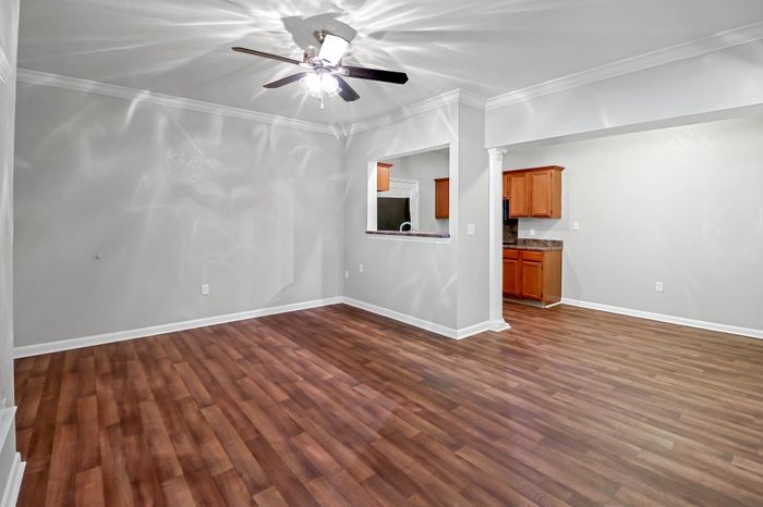 Chic open living space featuring elegant wood flooring and a sleek ceiling fan, seamlessly connected to a cozy kitchen area with warm wooden cabinetry.