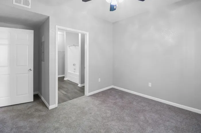Modern bedroom featuring plush carpet, ample natural light, and a connected bathroom with sleek flooring.