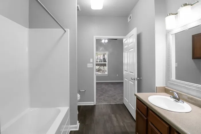 Inviting bathroom with modern fixtures adjacent to a sunlit bedroom, featuring sleek flooring and elegant design.