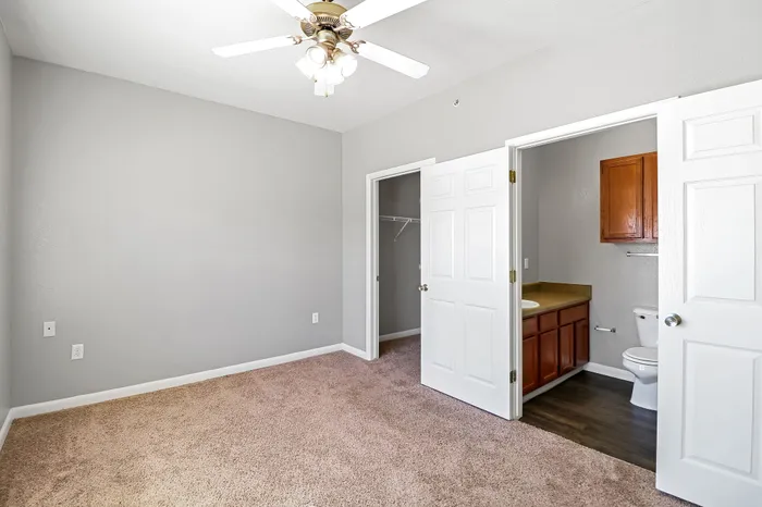 Bright, elegant bedroom with plush carpeting, modern ceiling fan, and walk-in closet attached to a stylish en-suite bathroom.