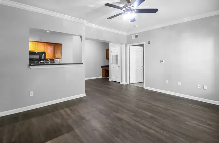 Modern apartment interior with elegant hardwood floors, open living space, and a stylish ceiling fan. Features a cozy kitchen with light wood cabinetry and black appliances, offering a seamless blend of comfort and style.