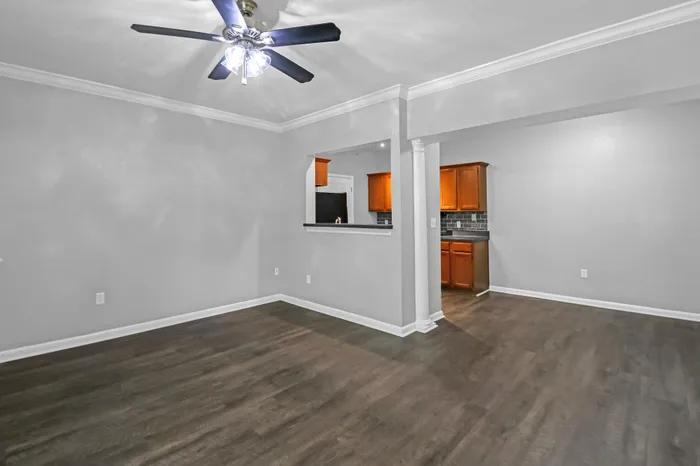 Spacious open-plan living area with elegant hardwood floors, modern ceiling fan, and stylish kitchen with warm wooden cabinets.
