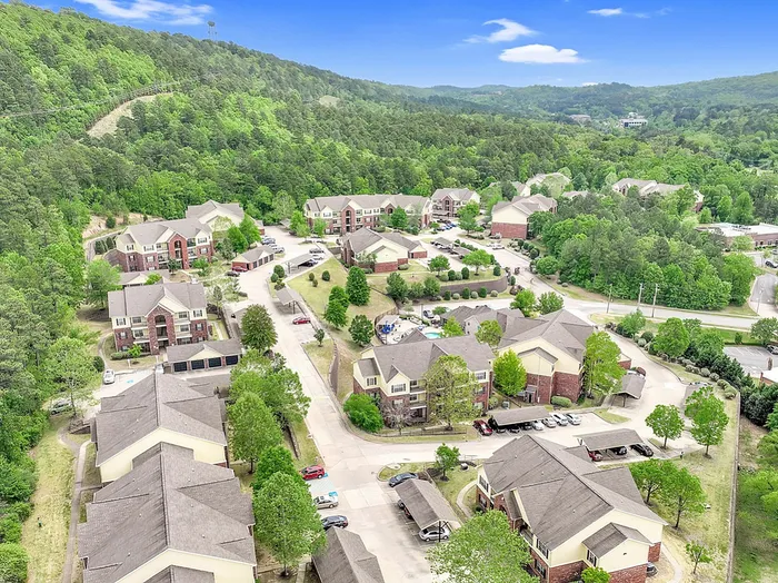 Charming aerial view of a lush wooded apartment complex surrounded by rolling hills, offering serene living amidst nature.