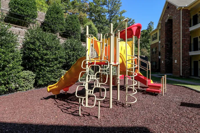 Vibrant playground with slides and climbing structures amidst lush greenery in a sunny residential complex.