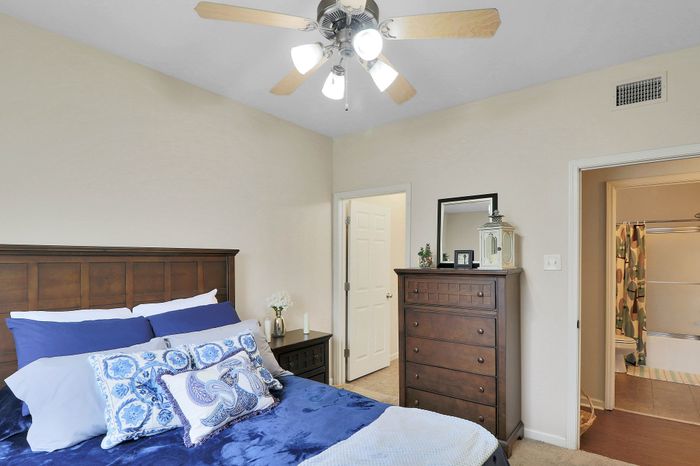 Elegant bedroom featuring plush pillows, rich wooden furniture, and a ceiling fan, leading to a stylish en-suite bathroom.