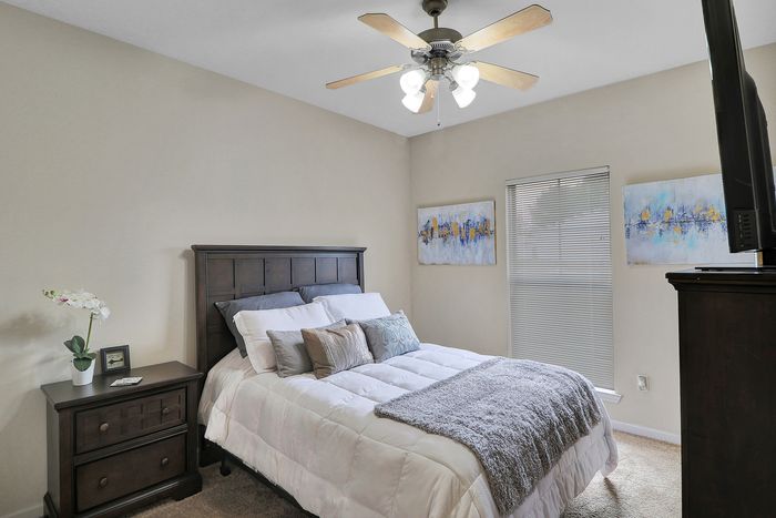 Cozy bedroom featuring an elegant double bed, modern ceiling fan, and stylish decor with abstract artwork and warm lighting.