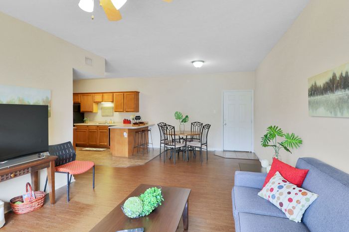 Inviting open-concept living space featuring a cozy lounge area, modern kitchen, and elegant dining set, enhanced by warm wooden flooring and vibrant decor.
