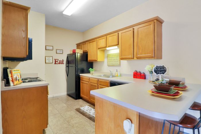 Inviting kitchen with warm wooden cabinetry, sleek black appliances, and a cozy breakfast bar with stylish dishware.