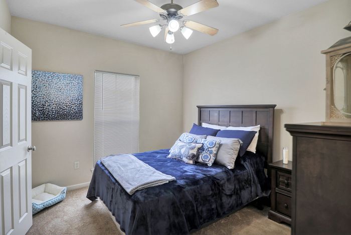Inviting bedroom with plush navy bedding, modern ceiling fan, and elegant nightstand, perfect for a restful retreat.