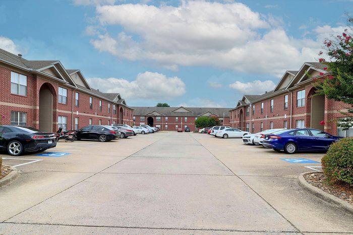 Charming brick apartment complex with ample parking, set against a stunning blue sky backdrop.