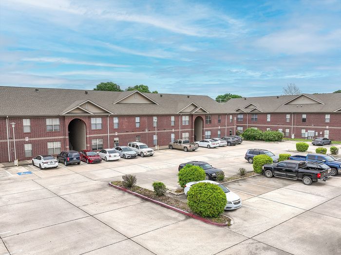 Inviting apartment complex with abundant parking and well-maintained landscaping under a bright blue sky.