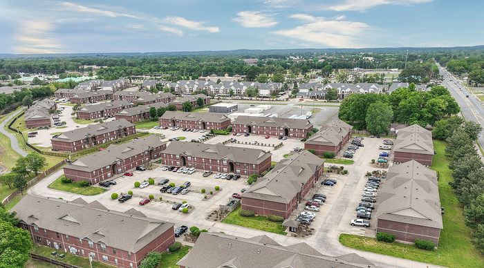 Expansive aerial view of a vibrant apartment complex with landscaped greenery and ample parking, set in a scenic suburban neighborhood.