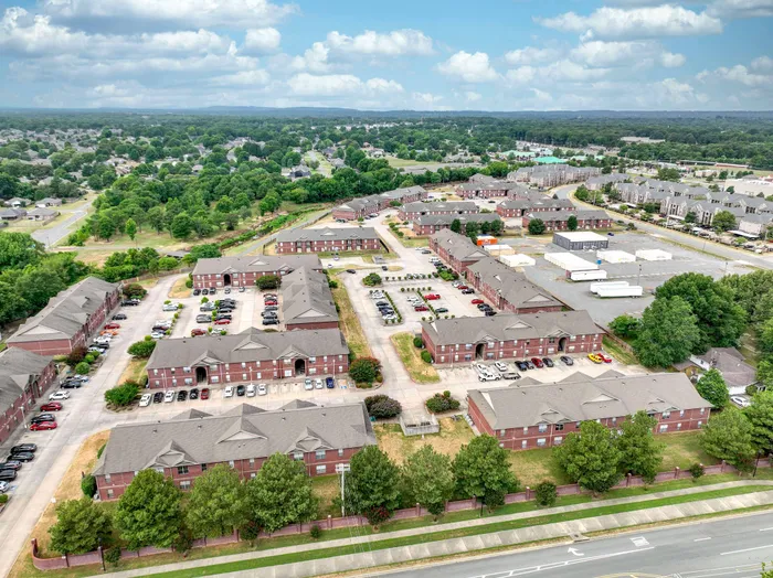 Aerial view of a charming apartment complex with red brick buildings, lush greenery, and spacious parking, set in a vibrant neighborhood with scenic surroundings.