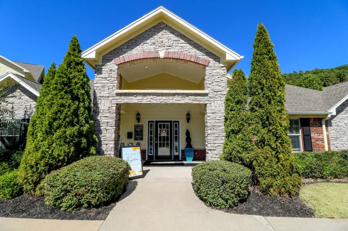 Charming leasing office with stone facade, nestled between lush greenery, welcoming residents with its elegant entrance.