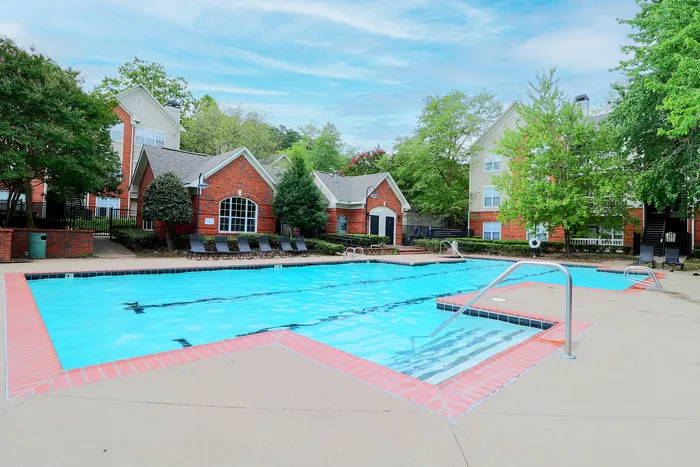 Luxurious apartment complex with a sparkling swimming pool and charming red-brick buildings surrounded by lush greenery.