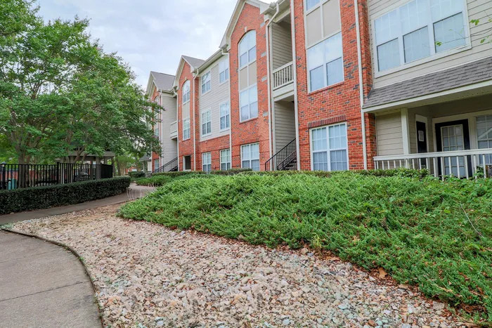 Charming apartment complex with modern brick facade, lush greenery, and inviting pathways creating a serene living environment.