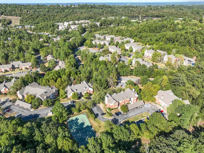 Aerial view of a charming residential community surrounded by lush greenery, featuring modern apartments and a tennis court.