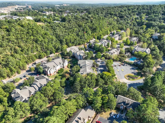 Lush aerial view showcasing a serene apartment community nestled among verdant greenery, featuring a sparkling swimming pool and ample parking.