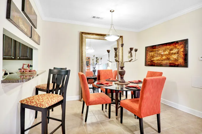 Inviting dining area with a glass-top table, vibrant red chairs, and a decorative centerpiece, complemented by a stylish bar counter with high stools for additional seating.