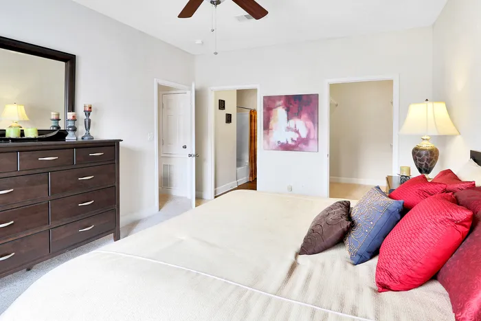 Elegant bedroom featuring a cozy bed adorned with vibrant pillows, a sleek dark wood dresser, and modern decor creating a warm and inviting ambiance.