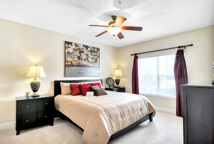 Inviting bedroom with elegant decor, featuring a cozy bed with vibrant cushions, ambient lighting, and large window for natural light.