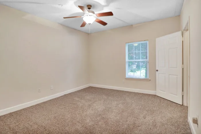 Bright and spacious bedroom with plush carpet, modern ceiling fan, and large window providing natural light.