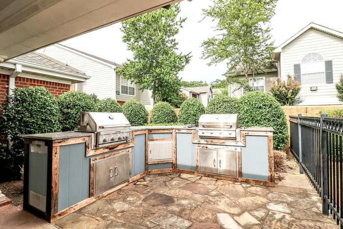 Charming outdoor patio with modern built-in grills, surrounded by lush greenery and elegant fencing, perfect for inviting summer barbecues.