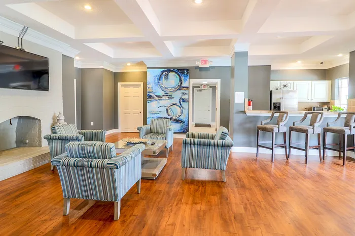 Inviting living room with elegant coffered ceiling, plush striped armchairs, and a sleek kitchen bar area.
