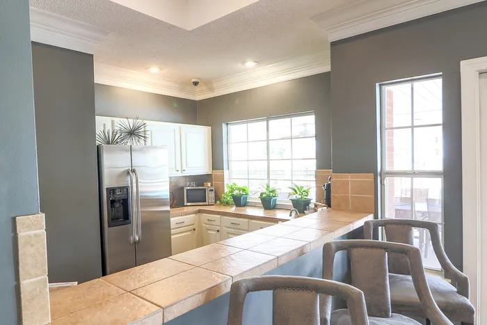 Charming open kitchen with a modern stainless steel fridge, elegant tile countertops, and large windows inviting natural light.