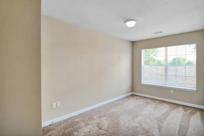 Bright and welcoming bedroom featuring plush carpet and a large, sunlit window offering peaceful views.