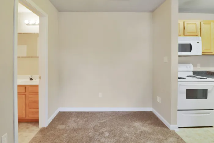 Bright apartment corner with plush carpeting, adjacent to a modern kitchen featuring sleek appliances and a cozy bathroom entrance.