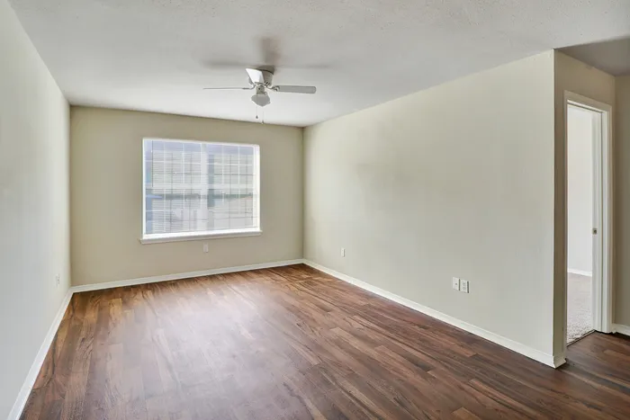 Bright spacious room with elegant hardwood flooring and large window, perfect for a modern living area. Ceiling fan adds comfort to this inviting space.