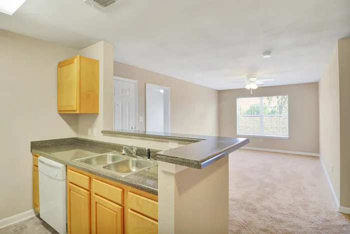 Bright and inviting open-concept kitchen and living room with modern wooden cabinetry and a large window flooding the space with natural light.