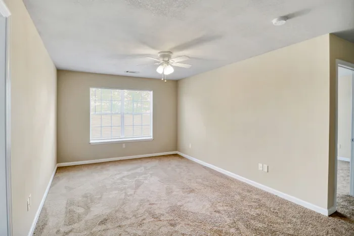 Spacious bedroom featuring soft carpet flooring, ample natural light from a large window, and a ceiling fan for comfort.