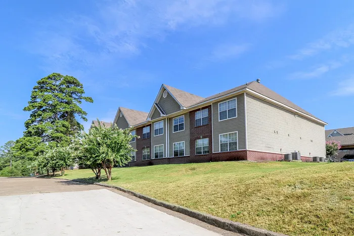 Charming two-story apartment building with brick and siding facade, surrounded by lush greenery and bright blue skies.