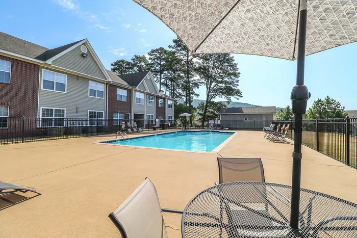 Inviting apartment complex with a sparkling outdoor swimming pool, surrounded by lounge chairs and shaded seating, perfect for relaxation and leisure.
