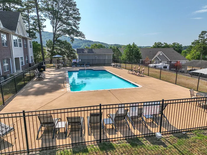 Inviting apartment complex with a sparkling outdoor pool, surrounded by lush greenery and a backdrop of scenic hills.