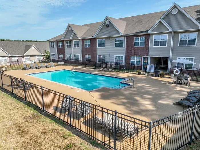 Inviting apartment community showcasing a sparkling swimming pool surrounded by comfortable lounge chairs, perfect for relaxation and leisure in a serene setting.
