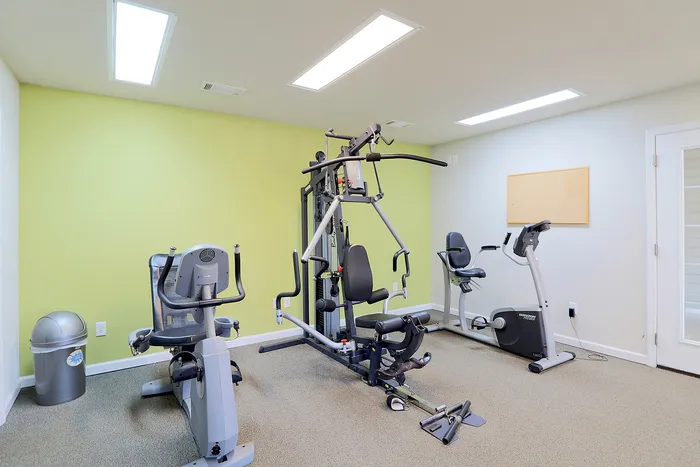 Modern fitness room with state-of-the-art exercise equipment, including a multi-gym, stationary bike, and elliptical machine against a vibrant yellow accent wall.