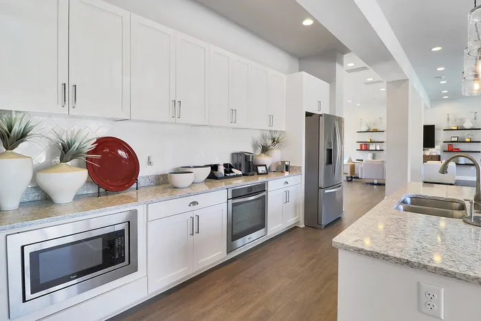 Sleek modern kitchen with elegant granite countertops, stainless steel appliances, and stylish open shelving flowing into a bright living area.