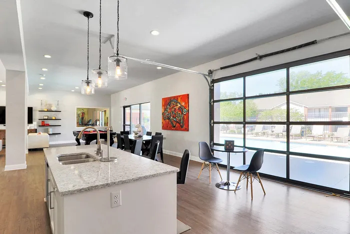 Modern open-plan interior with stylish kitchen island, chic lighting, and expansive glass doors overlooking a poolside view.