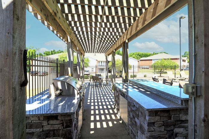 Outdoor grill area featuring sleek granite countertops under a charming pergola, perfect for entertaining and enjoying sunny days with a view of the vibrant community courtyard.