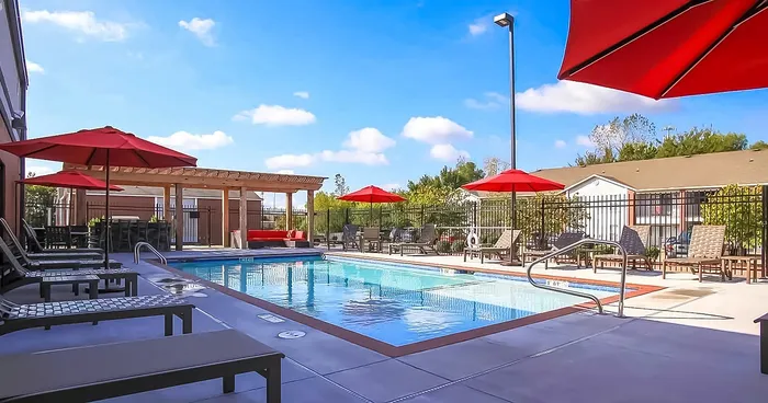 Inviting outdoor pool area with red umbrellas, sun loungers, and a shaded pergola, perfect for relaxation and leisure.