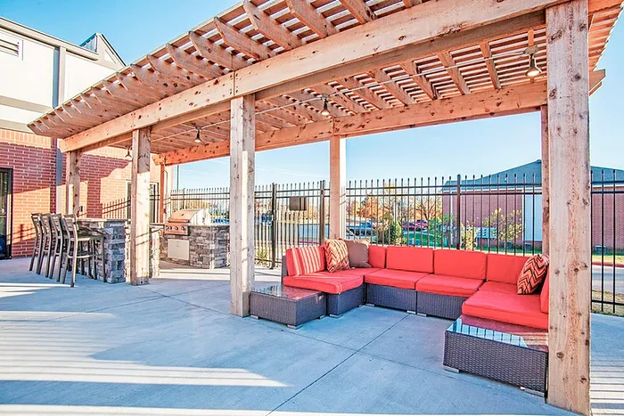 Inviting outdoor patio with wooden pergola, cozy red cushioned seating, and modern grilling area, perfect for entertaining.