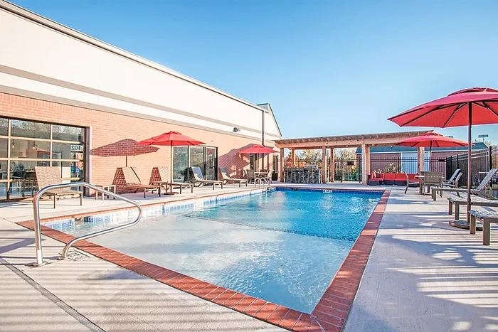 Inviting outdoor pool surrounded by stylish lounge chairs and vibrant red umbrellas, perfect for relaxation and leisure.