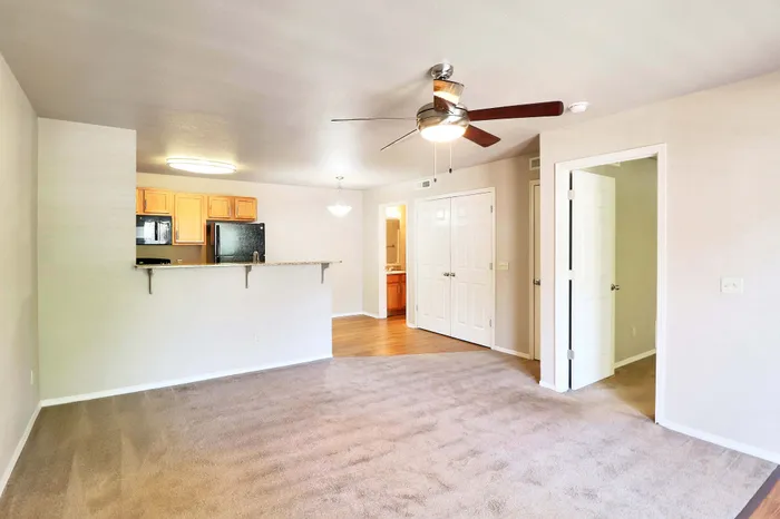 Bright and inviting open-concept living room with cozy carpeting, adjacent to a modern kitchen with wooden cabinets and sleek appliances. Ideal for comfortable living and entertaining.